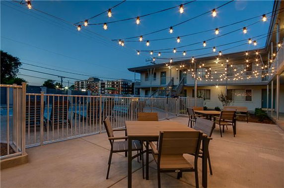 Outdoor area with string lights, chairs, tables, and a gated swimming pool in the background.