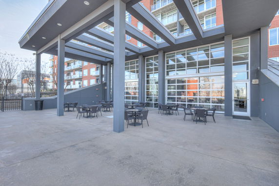 Outdoor view of a multi-story building with large glass windows and a patio area with tables and chairs.