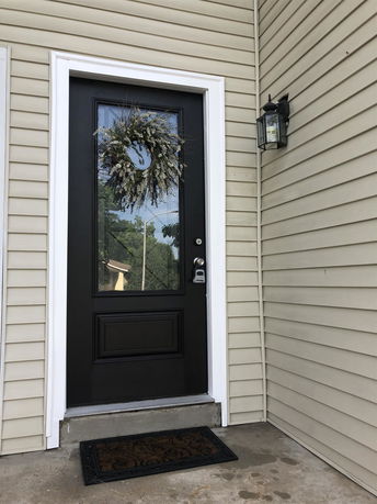 Front view of a house door with a wreath, accompanied by a light fixture.