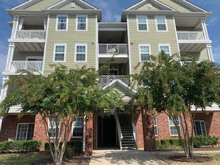 Front view of a multi-story residential building with balconies and brick facade on the ground floor.