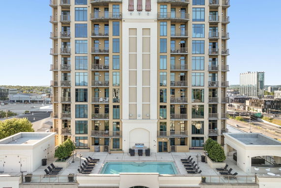 Front view of a multi-story building with balconies and a swimming pool area.
