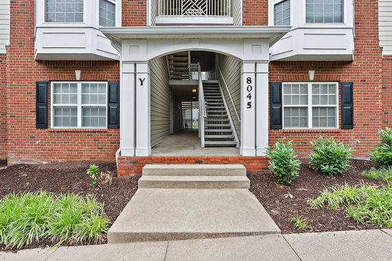 Front view of a multi-story building entrance with brick facade and outdoor staircase.
