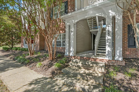 Front view of a building with stairs leading to the entrance, brick exterior and surrounding greenery.