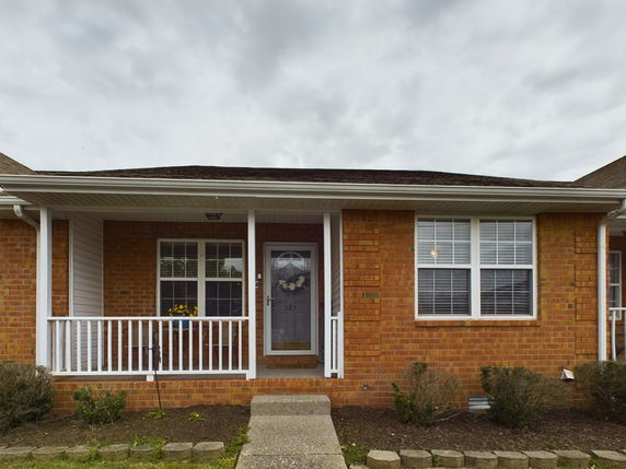 Front view of a single-story brick house with a white railing porch.