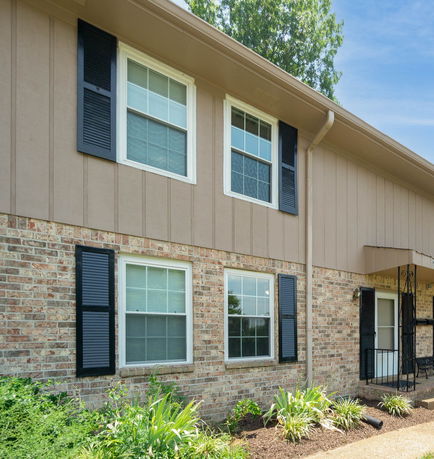 Front view of a two-story house with brick and wooden exterior and black window shutters.