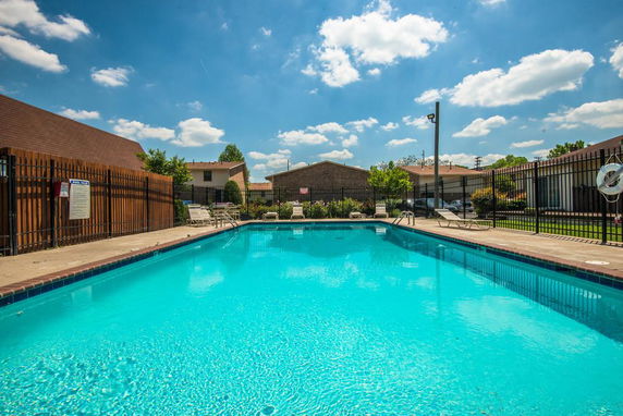 Outdoor swimming pool with surrounding fence and nearby buildings.