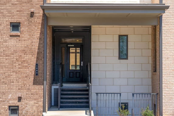 Front entrance of a building with brick and stone facade and a staircase leading to a black door.