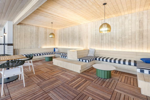 Indoor recreation area with wooden seating and tables, pendant lights, and wood paneling.