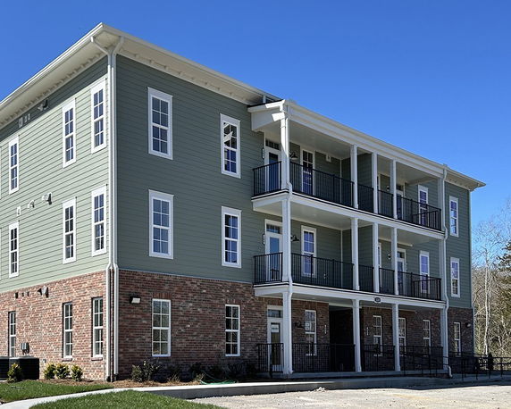 Front view of a multi-story apartment building with green siding and brick lower level.