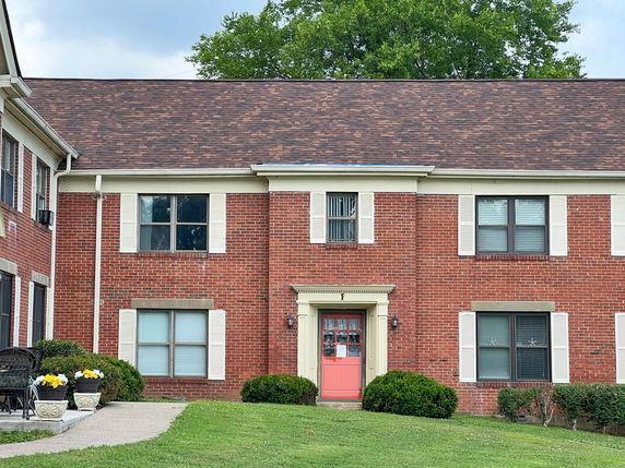 Front view of a two-story brick house with a red door and white window shutters.