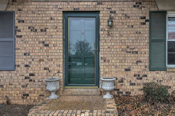 Front view of a brick house with a green door and two decorative planters.