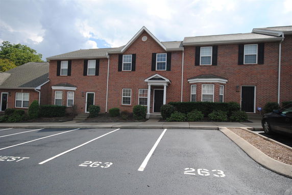 Front view of a brick townhouse building with black shutters and a designated parking area in front.