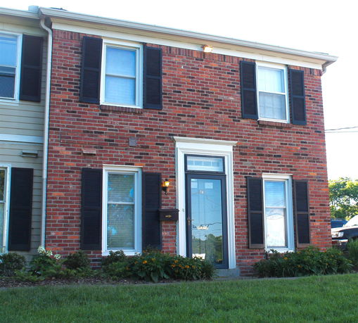 Front view of a two-story brick house with dark shutters.