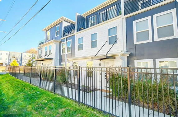 Front view of a multi-story residential building with multiple balconies and a fenced sidewalk.