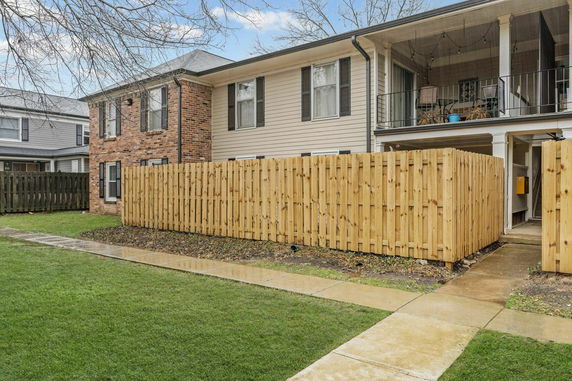 Front view of a two-story house with a combination of brick and siding exterior, featuring a wood fence and a covered balcony.