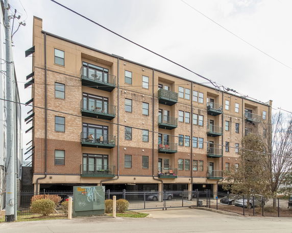 Front view of a multi-story apartment building with balconies and parking area.