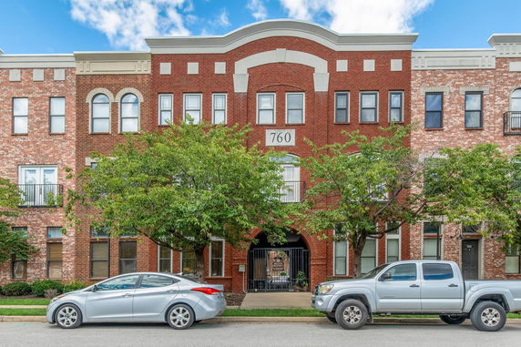 Front view of a multi-story brick building with two cars parked in front.