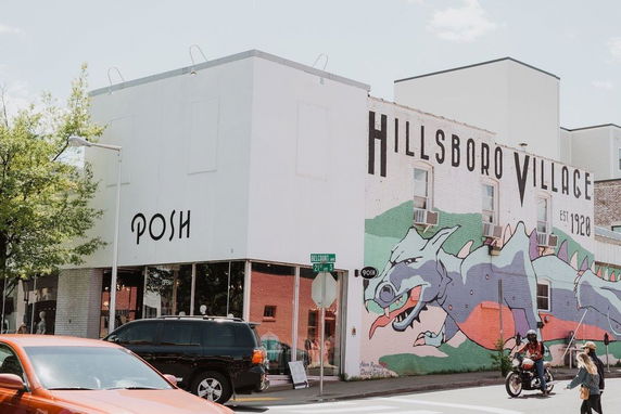 Front view of a building with large signage 'Hillsboro Village' and street art on the wall.