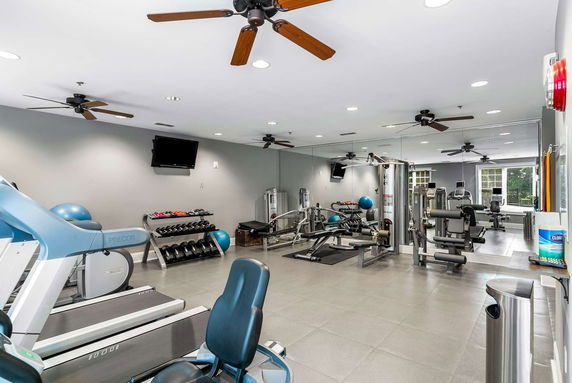 Room equipped with gym equipment, mirrors, and ceiling fans.