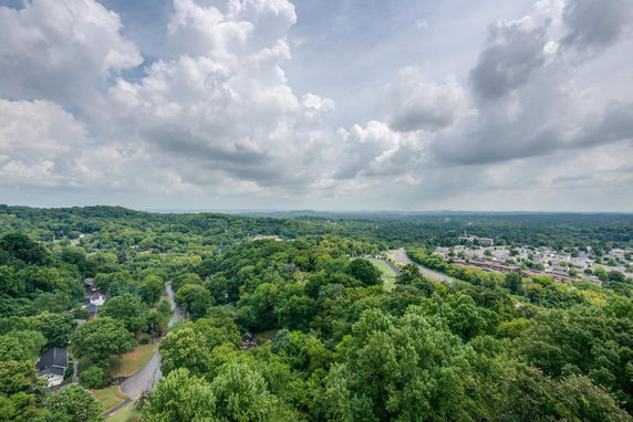 Wide angle view of a landscape with trees, roads, and distant buildings under a cloudy sky.