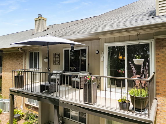Elevated balcony with outdoor seating and umbrella, attached to house exterior.