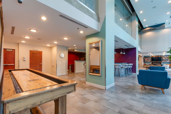 Interior view of a clubhouse with a shuffleboard table, seating area, and bar.