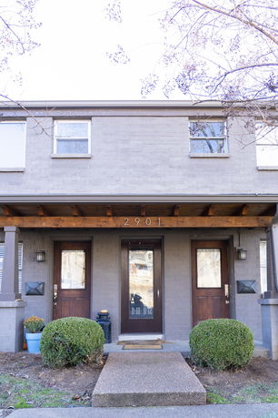 Front view of a two-story house with two entrance doors and a wooden canopy.