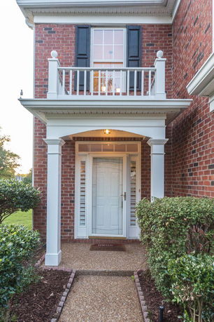 Front view of a brick house entrance with white columns and a balcony.