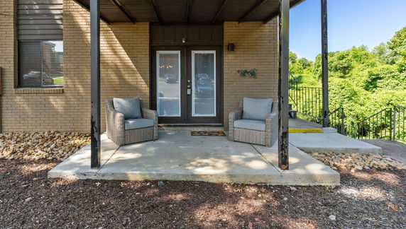 Front view of a house entrance with double glass doors and two chairs on a covered porch.