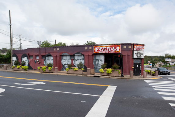 Exterior view of a comedy club with a mural of faces on the wall.