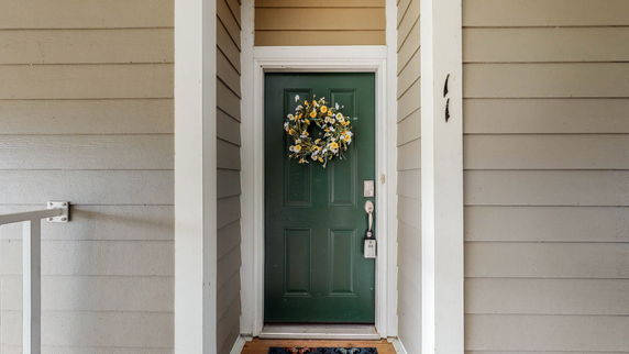 Front view of a house entrance with a green door and decorative wreath.