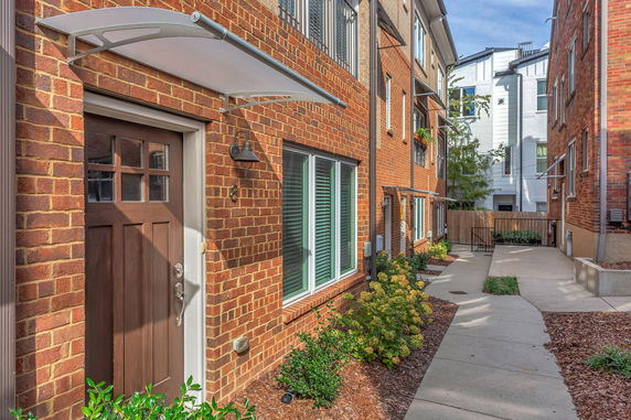Front view of a brick residential building with a wooden door and windows, featuring a small awning above the entrance.