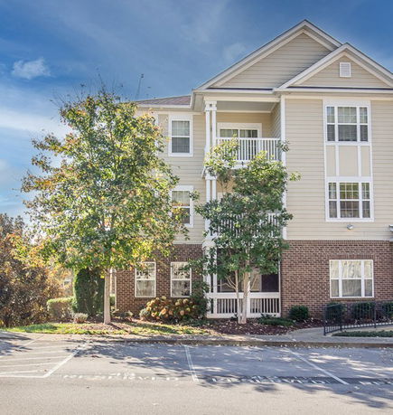 Front view of a multi-story residential building with balconies and brick lower facade.
