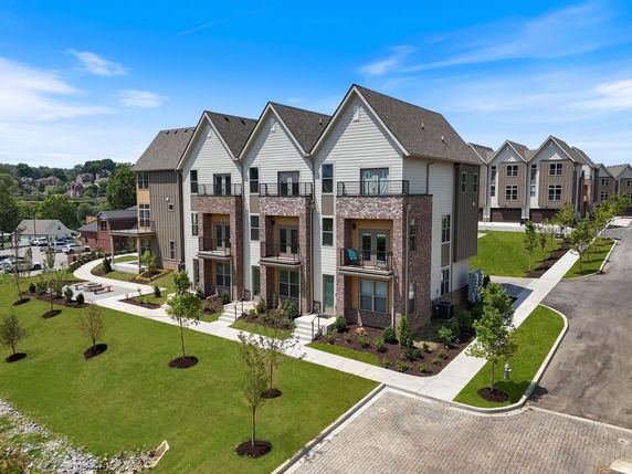 Front view of a multi-story residential building with multiple gables and balconies, surrounded by landscaped pathways and lawn.