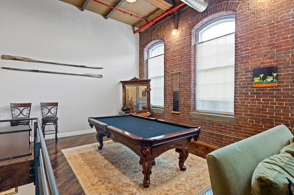 Room with a pool table and high chairs against a brick wall.
