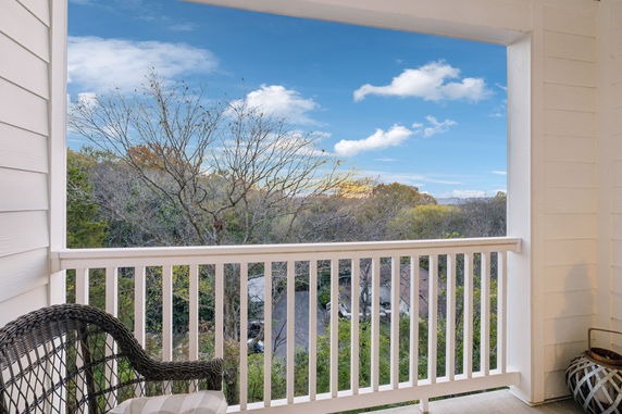 View from a balcony overlooking trees and rooftops in the distance under a blue sky.