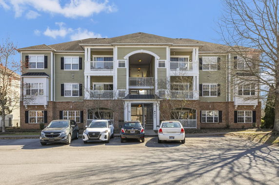 Front view of a three-story apartment building with balconies and a parking area.