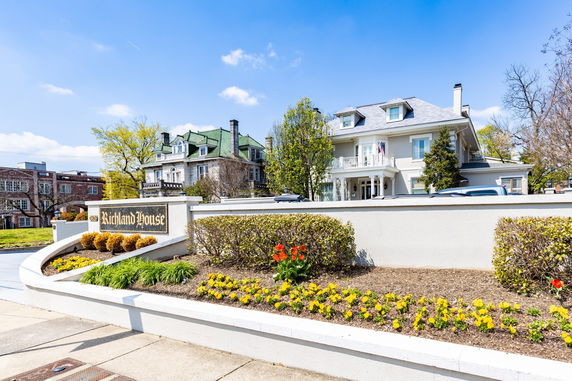 Front view of a large multi-story house with a balcony and distinctive roof design.