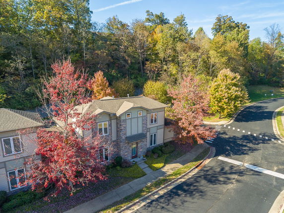 Aerial view of a two-story house near a curved road, surrounded by trees with autumn foliage.