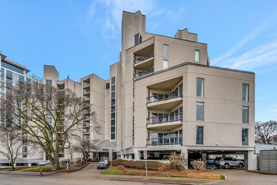 Front view of a multi-story apartment building with balconies and parking area.