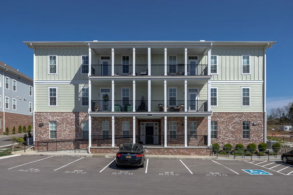 Front view of a three-story residential building with balconies and a parking area.