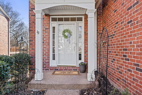Front entrance of a brick house with white columns and a decorative wreath on the door.