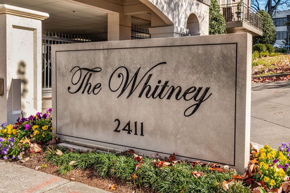 Front view of a building entrance with a sign reading 'The Whitney 2411' and surrounding landscaping.