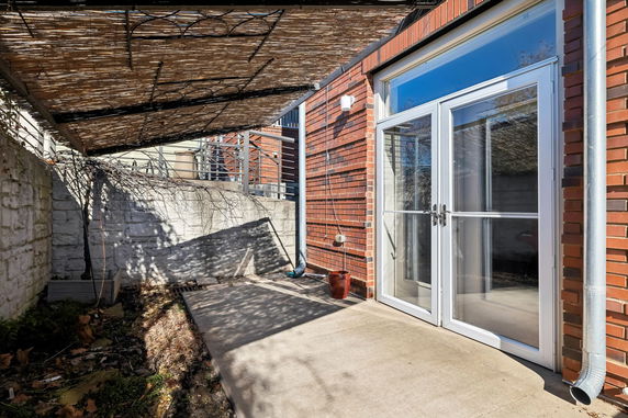 Exterior view showing a brick wall with a glass double door leading to a patio area.