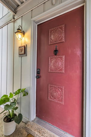 Front view of a house entrance with a red door and wall-mounted light.