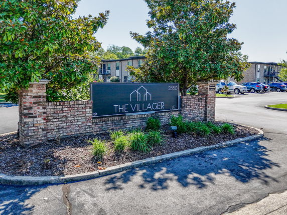 View of an apartment complex entrance with a sign and trees.