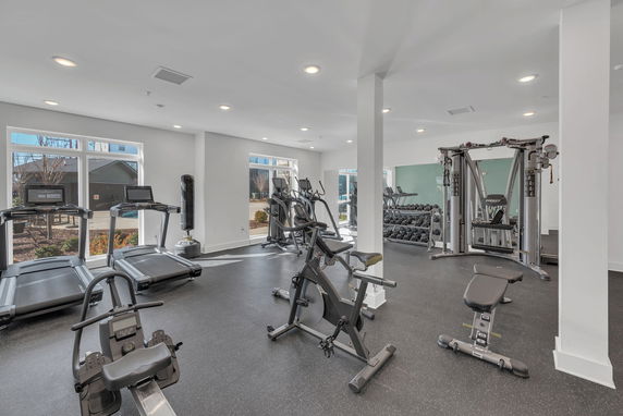Interior view of a gym with various exercise equipment, including treadmills, exercise bikes, and a weightlifting area.