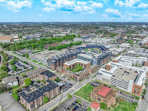 Aerial panoramic view of a cityscape featuring multiple residential and commercial buildings, parking areas, and a sports stadium.