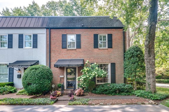 Front view of a two-story brick townhouse with black shutters and an awning over the entrance.