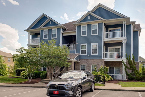 Front view of a three-story apartment building with balconies and a parked car.